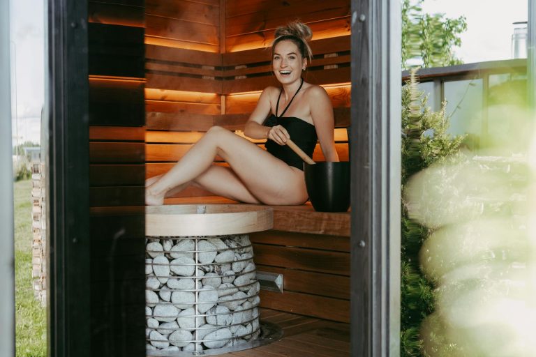 A woman enjoying a relaxing moment inside a modern sauna, showcasing wooden design and sauna stones.